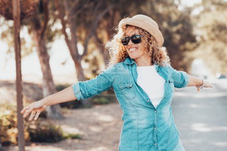 Portrait of wonderful female model with curly blonde hair expressing energy on a good day in Europe. Beautiful curly woman smiling and walking with trees behind her.