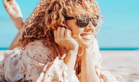 Photo for Side view of a beautiful woman lying on the beach. Blonde woman with curly hair blowing in the wind relaxes looking and smiling. - Royalty Free Image