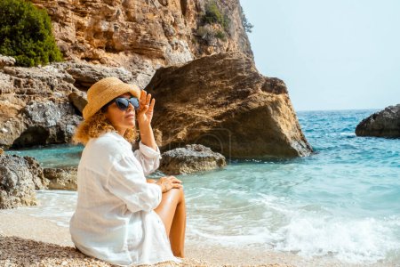 Touristin sitzt am tropischen Strand und genießt die Freizeitaktivität im Freien allein und trägt einen Strohhut. Menschen und Lebensstil im Sommerurlaub. Erwachsene Frauen entspannen in landschaftlich reizvoller Umgebung