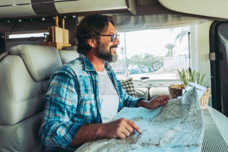Glücklich erwachsener Mann lächelt in einem Wohnmobil mit Papier-Karte Führer Reiseziele Urlaub zu planen. Vanlife Lebensstil alternative Menschen. Leben ohne Netz und Reisen. Van leben moderne Menschen