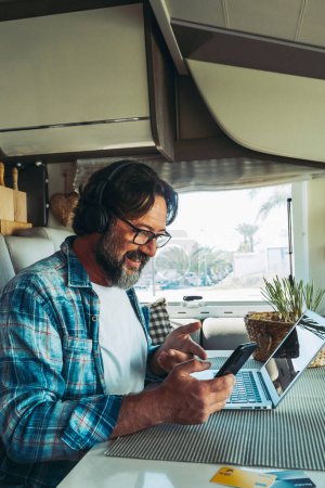 Traveler moderne Online-Menschen Job Business Lifestyle. Ein glücklicher, reifer Mann mit Telefon und Computer in einem Wohnmobil. Urlaubsreisen und Roaming-Verbindungstechnik