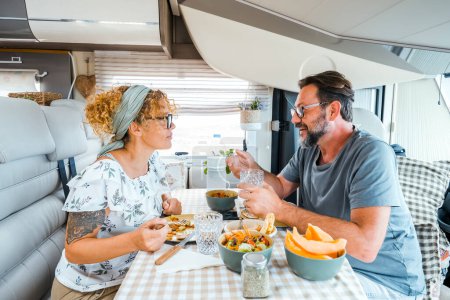 A happy couple spending time together having fun during vegetarian lunch inside a camper. People talking and sharing projects organizing the next destination.