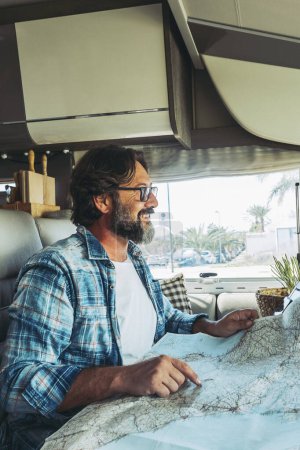 Happy mature man smilng inside a camper camping car using paper map guide to plan destinations holiday. Vanlife lifestyle alternative people. Living offgrid and travel. Van life modern people