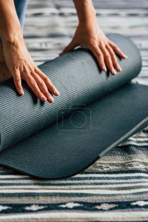 Téléchargez les photos : Gros plan de la femme fermant son tapis de yoga après avoir terminé une séance d'entraînement de mode de vie sain seul à la maison ou au gymnase. Concept de sport fitness style de vie femmes. Entraînement intérieur routine quotidienne - en image libre de droit