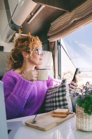  tourist woman admire the beach inside her modern camper van and use mobile phone. Summer transport holiday vacation people with motor home. Alternative home and lifestyle. Vanlife lady leisure