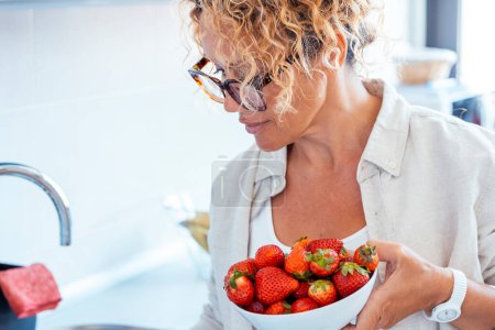  mujer de mediana edad en casa con tazón fresco de fresas rojas, frutas de temporada. Concepto de pérdida de peso y recuento de déficit calórico. Comer dietas naturales personas sanas estilo de vida femenino. Frutos de fresa