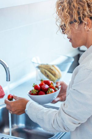 Estilo de vida saludable mujer en el lavado en casa limpieza de fresas rojas en el fregadero en la cocina blanca interior. Las personas y la nutrición saludable desayuno con frutas y bajas calorías. Alimentación y nutrición