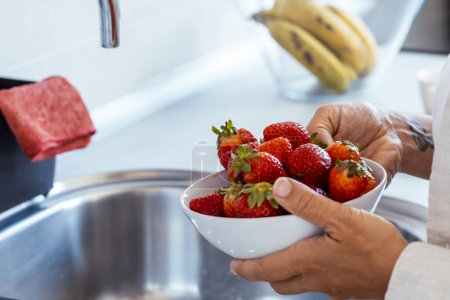 Frau mittleren Alters zu Hause mit frischen Schüsseln mit roten Erdbeeren, saisonalen Früchten. Konzept der Gewichtsabnahme und Kaloriendefizit zählen. Natürliche Ernährung gesunde Menschen weiblichen Lebensstil. Erdbeerfrüchte