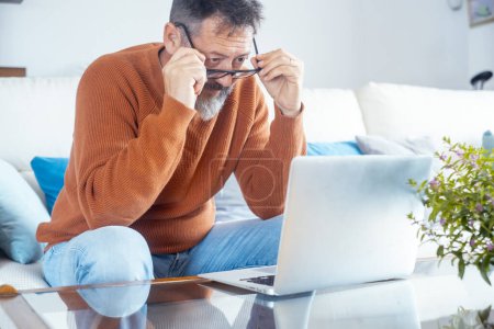 professional adult freelance looking on laptop screen with thoughtful expression. People and eyesight problems with glasses. Thinking to solve problems. Mature male and eyewear using computer