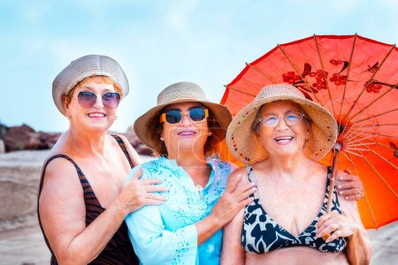 Group of women friends aged smiling and posing for a photo in summer outdoor leisure activity together in friendship. Colorful accessories and sunglasses. Holiday vacation elderly people females ladies