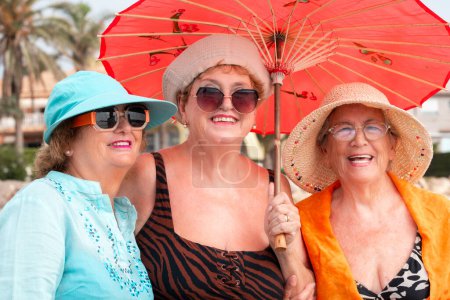 Group of women friends aged smiling and posing for a photo in summer outdoor leisure activity together in friendship. Colorful accessories and sunglasses. Holiday vacation elderly people females ladies