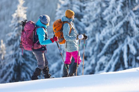 Two women walk through the snow on a winter hike, two women in the mountains in winter, hiking equipment, snowshoe