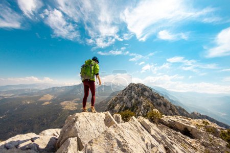 Photo for Woman climber with a backpack and a helmet in the mountains. A girl with a backpack walks along a mountain range. adventure and mountaineering concept. hiking with a backpack in the mountains. - Royalty Free Image