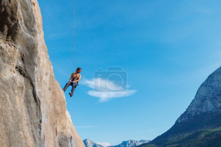 Photo for Rock climber descends from a route, a climber hangs on a rope against the sky, rock climbing routes in a cave, a man rappels down a rope - Royalty Free Image