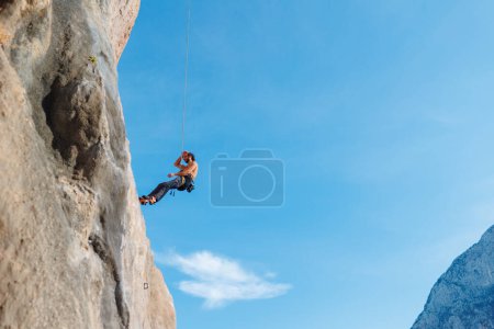 Photo for Climber with rope. A young man is engaged in rock climbing, an athlete descends from above on a background of blue sky on a rope. - Royalty Free Image