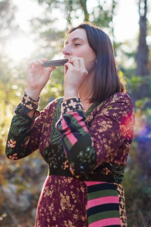 Photo for Young girl plays the harmonica in the forest. the girl loves to play the harmonica. girl in the forest. - Royalty Free Image