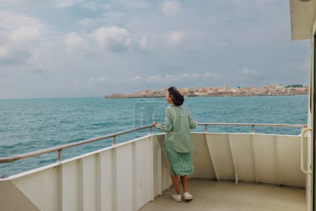 Una joven mujer se para en la cubierta de un crucero y mira a la ciudad. La chica está viajando. viaje en barco. Vista de la ciudad y puerto en la ciudad de Akko (Acre), Israel. viajes y aventura.