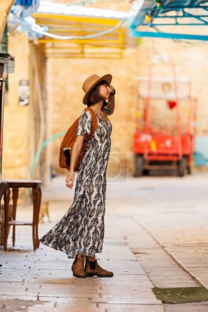 Hermosa chica viajera con un sombrero y una mochila explorando la histórica ciudad de Acre en Israel. viajes y aventura