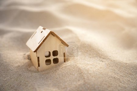 Kleines Spielzeughaus in tiefem Sand mit Sanddünen und Sonnenstrahlen. Immobilien, Naturkatastrophen und Kataklysmen, Sandstürme. Kopierraum