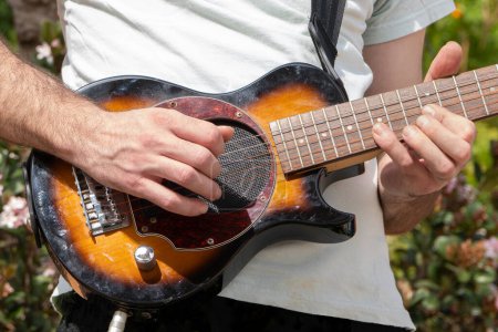 Guitarra eléctrica pequeña en manos del guitarrista jugando al aire libre de cerca