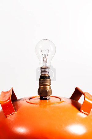 Foto de Primer plano de una bombilla no iluminada colocada en la válvula de un tanque de gas doméstico naranja sobre fondo blanco. - Imagen libre de derechos