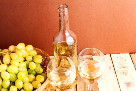 Téléchargez les photos : Vue de dessus nature morte avec un panier plein de raisins, une bouteille et deux verres avec du vin blanc sur une table rustique en bois. - en image libre de droit