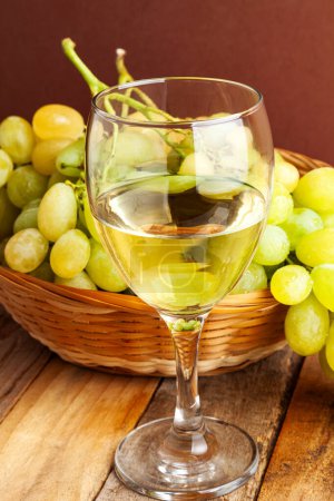 Téléchargez les photos : Tournage vertical d'un verre de vin blanc devant un panier avec des raisins sur une table en bois. - en image libre de droit