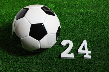 A classic black and white soccer ball over a green grass filed next to a wooden number 24.