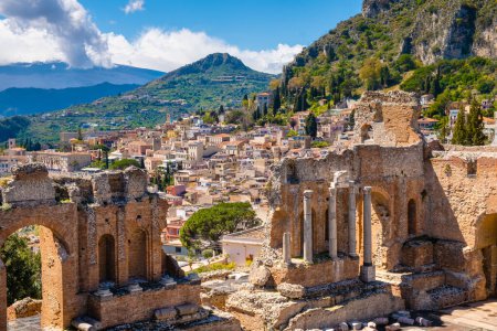 Taormina auf Sizilien, Italien. Ruinen des antiken griechischen Theaters, der mit Wolken bedeckte Ätna. Taorminas Altstadt und die Berge im Hintergrund. Beliebtes Touristenziel auf Sizilien.
