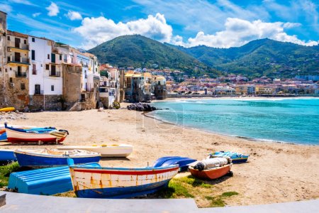 Fishing boats on beach of Cefalu, medieval town on Sicily island, Italy. Seashore village with historic buildings, clear turquoise sea water and mountains. Popular tourist attraction near Palermo.