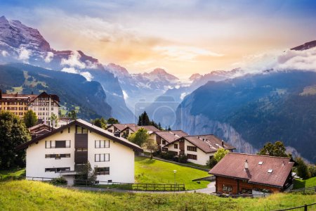 Wengen town in Switzerland at sunset. View over Swiss Alps near Lauterbrunnen valley. Typical Swiss houses in Wengen. Mountain peaks of Eiger and Jungfrau covered with snow and clouds.