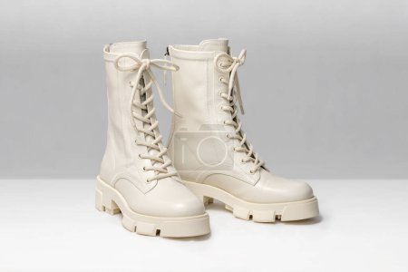 Photo for Pair of stylish white boots for women on light gray background. Trendy military beige boots on high platform with laces. Female fashion and shoes still life. - Royalty Free Image