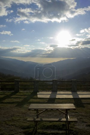 Photo for Picnic table with views of the Jerte Valley at sunset in winter vertically with sun between clouds - Royalty Free Image
