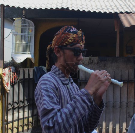 the expression of a man in a traditional costume from Java while blowing a flute during the celebration of the 72nd Indonesian Independence Day