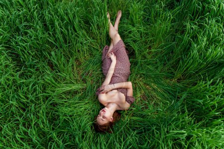 A young girl in a beautiful dress lies in the green grass. A happy girl enjoys silence, loneliness and nature