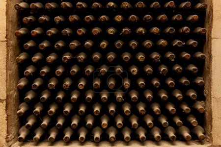 Photo for Old bottles of wine stacked in rows in the cellars of a winery - Royalty Free Image