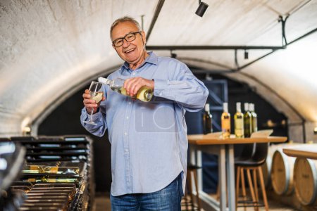 Photo for Portrait of senior man who owns winery. He is examining quality in his wine cellar. Industry wine making concept. - Royalty Free Image