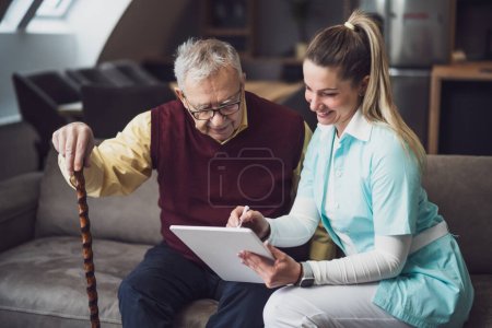 Nurse home caregiver is assisting old man at his home. Professional health support for elderly people.