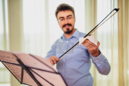 Téléchargez les photos : Homme jouant du violon à la maison. Il colophane un arc de violon. - en image libre de droit