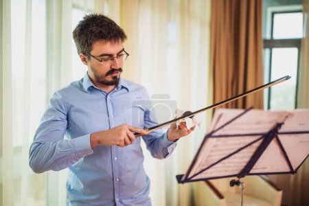 Téléchargez les photos : Homme jouant du violon à la maison. Il nettoie son instrument.. - en image libre de droit