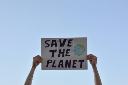 Foto de Manos sosteniendo un cartel con el cielo azul en el fondo para luchar contra el cambio climático. Concepto de calentamiento global y medio ambiente - Imagen libre de derechos