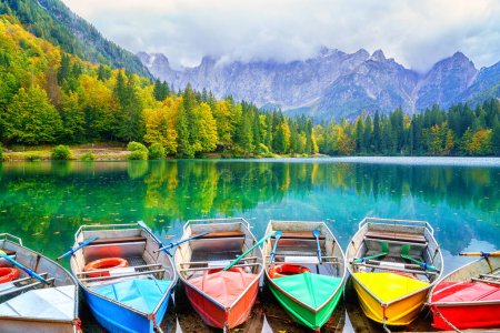 Téléchargez les photos : Laghi di Fusine lac inférieur, Tarvisio, Italie. Paysage d'automne incroyable avec des bateaux de plaisance dans l'eau et la forêt colorée entourée par la chaîne de montagnes Mangart, arrière-plan de voyage en plein air - en image libre de droit