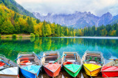 Laghi di Fusine inferior lake, Tarvisio, Italy. Amazing autumn landscape with pleasure boats in the water and colored forest surrounded by Mangart mountain range, outdoor travel background Poster #679491324