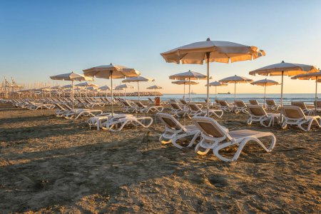 Téléchargez les photos : Vue sur la plage de sable Larnaca au lever du soleil, station touristique, Chypre. Paysage marin pittoresque avec parasols et chaises longues, arrière-plan de voyage, concept de vacances d'été - en image libre de droit