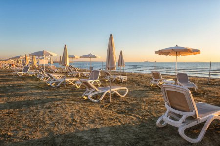Foto de Hermosa playa de arena con accesorios de playa blanca, mar tranquilo y cielo azul con nubes en suave luz de la mañana, paisaje marino, vacaciones de verano y concepto de viaje, Larnaca, Chipre - Imagen libre de derechos