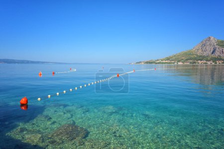 Adriatic seacoast, beach with crystal clear water of the sea and serene blue sky in the morning, Omis, Croatia, Dalmatia region. Outdoor travel background, summer holidays concept