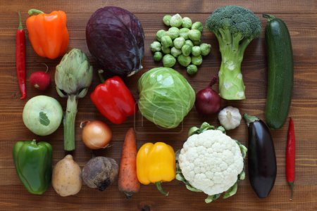 Vegetables on a brown wooden table. View from above. Closeup. Paprika, broccoli, Brussels sprout, kohlrabi, cauliflower, cabbage, red cabbage, squash, artichoke, eggplant, potato, beet, radish, carrot, onion, garlic, purple onion, hot red peppers.