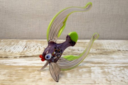 Figurine of fantasy fish made from glass on rough wooden background front view