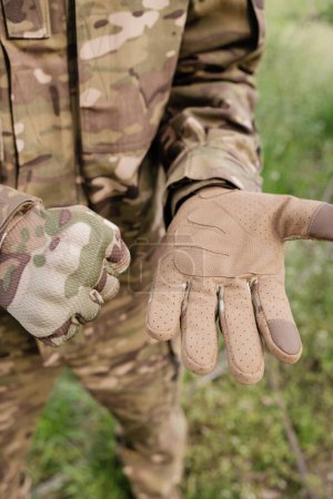 Vorbereitung auf den Einsatz: Nahaufnahme getarnter taktischer Handschuhe, die von Militärpersonal befestigt werden
