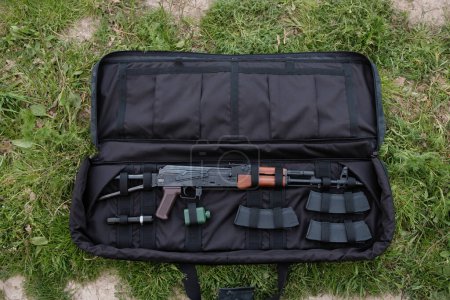 Foto de Funda de pistola descubierta con AK-47, cargadores y linterna tumbados en el suelo negro - Imagen libre de derechos